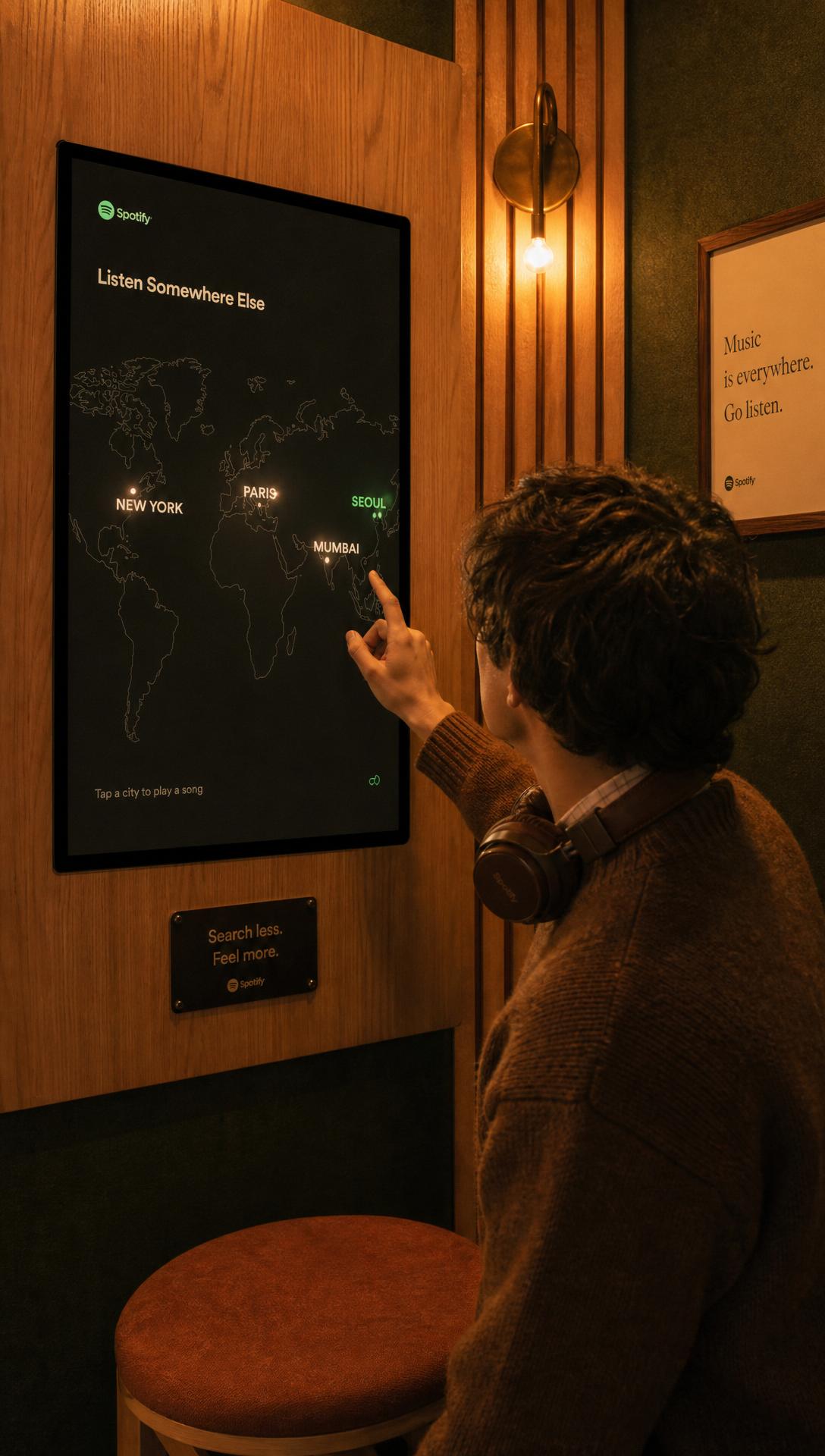 A visitor inside the booth touching a warm-lit screen showing a world map with New York, Paris, Seoul and Mumbai marked